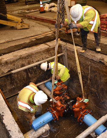 Three contractors lower a valve into a excavation below street level.